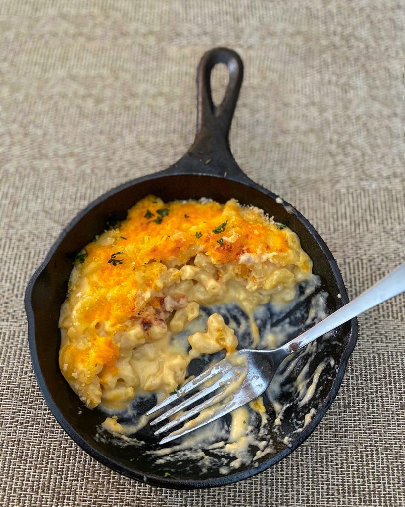 A half eaten cast iron filled with creamy Mac and cheese on a placemat with a fork sitting diagonally on the cast iron