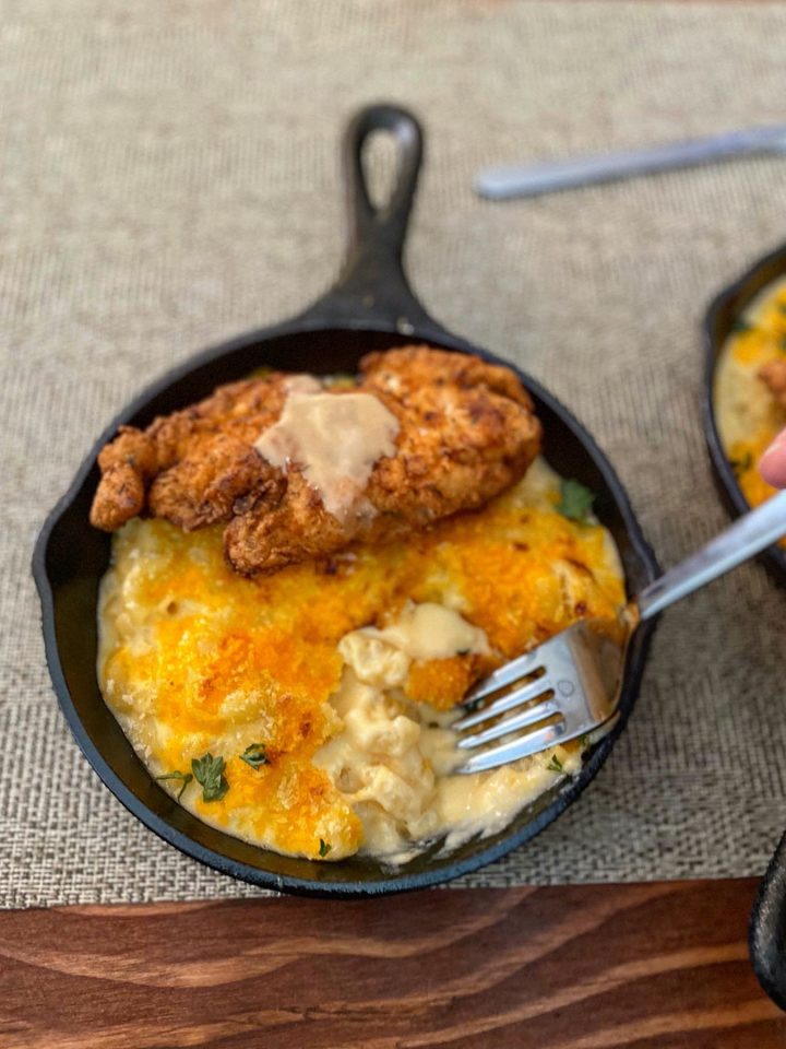 Cutting into the crispy crust of the Mac and cheese with a fork to reveal a creamy interior, topped with crispy fried chicken and maple butter
