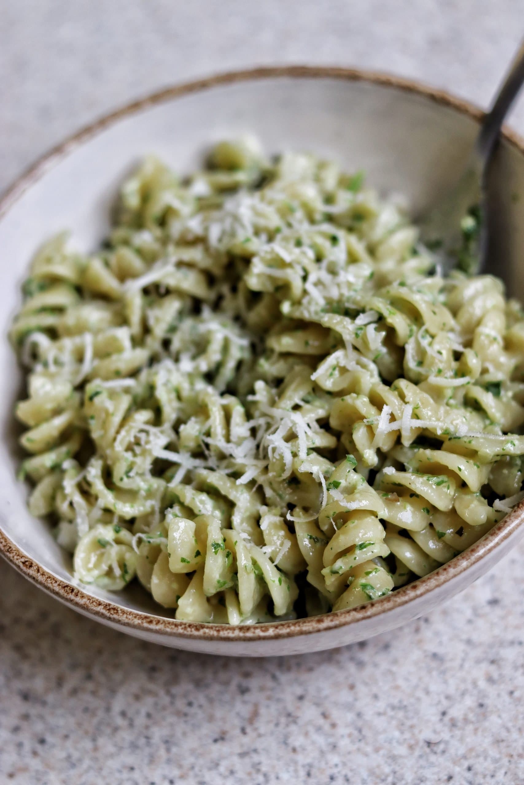 A bowl of the final product of the 4 ingredient pesto pasta with a fork out of the side of the bowl.