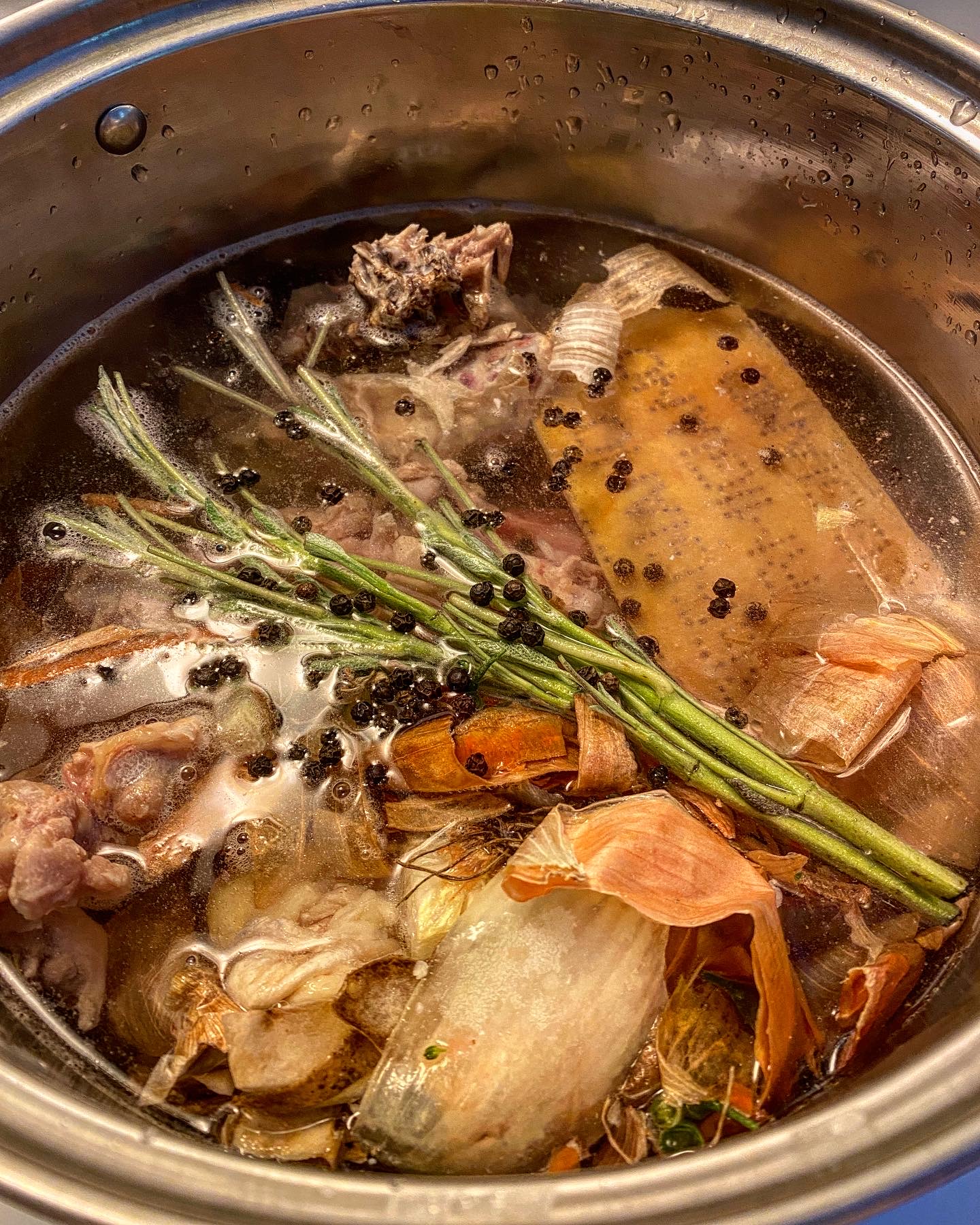 A pot filled with water and lots of vegetable scraps, herbs and chicken bones for making stock.
