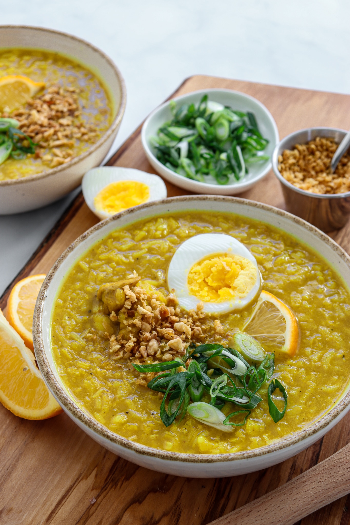 2 bowls loaded with a rich Arroz Caldo recipe - topped with a hard boiled egg, green onion, crispy fried garlic and a lemon wedge.