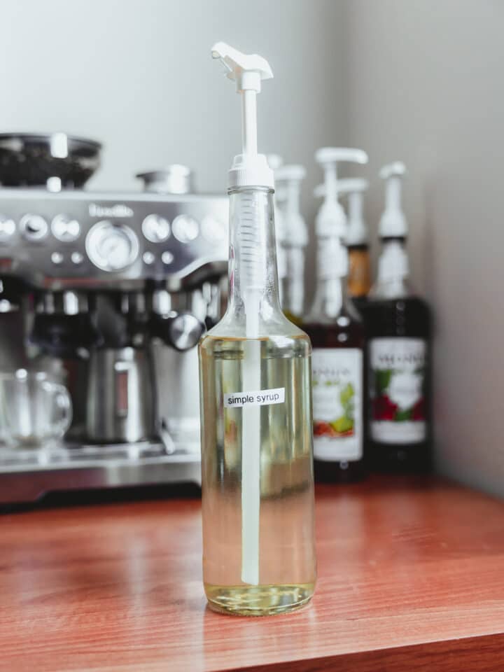 A bottle of homemade simple syrup in front of an espresso machine